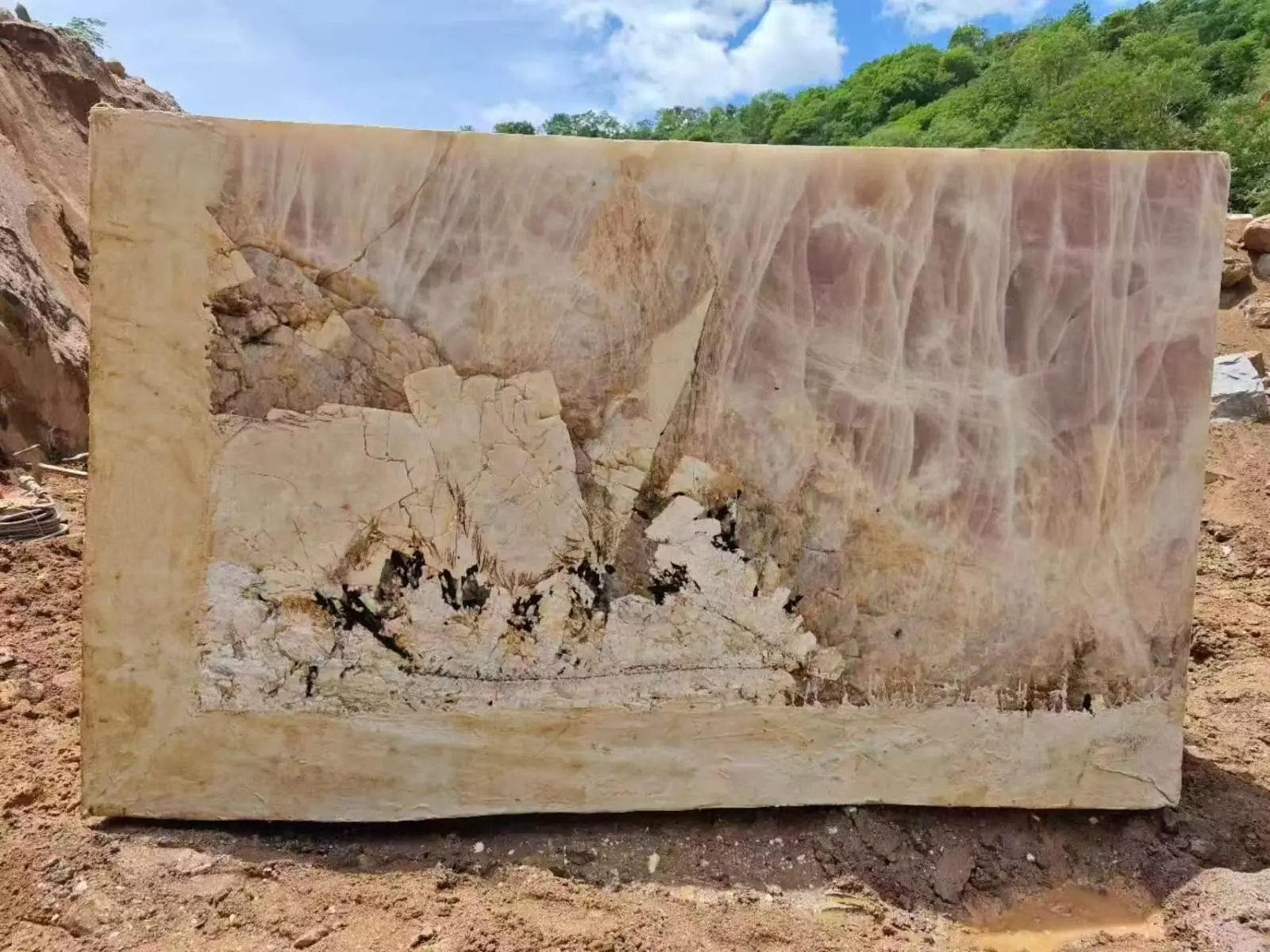 Large marble block with cream and pink natural veining in quarry setting